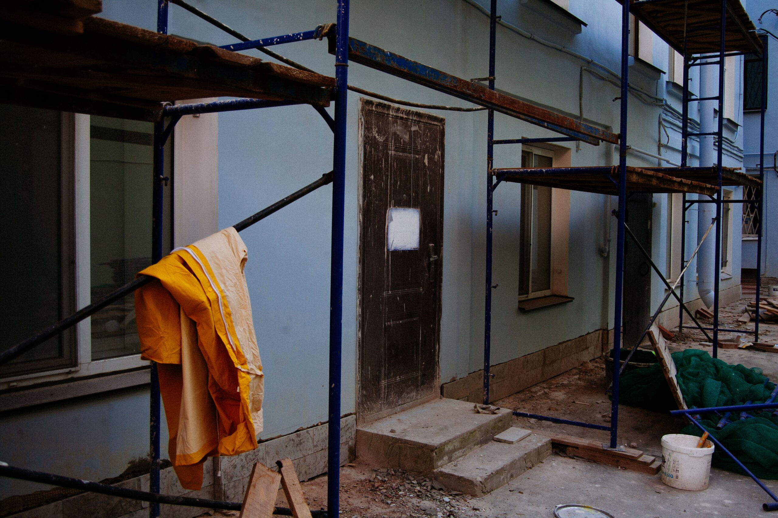 service-1 Exterior of renovated house with blue walls and entrance door behind scaffolding with wooden platforms in megapolis